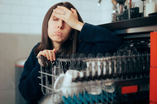 Woman holding head in frustration as she looks at the top rack of her broken dishwasher.